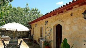 A courtyard with a stone wall, a wooden door, and a table with chairs under a white umbrella. - Quaint Holiday Home in Pasalites with Garden near Perama (Mylopotamos)