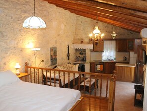 Une chambre à coucher avec un lit en bois, un petit bureau et, au fond, une kitchenette.