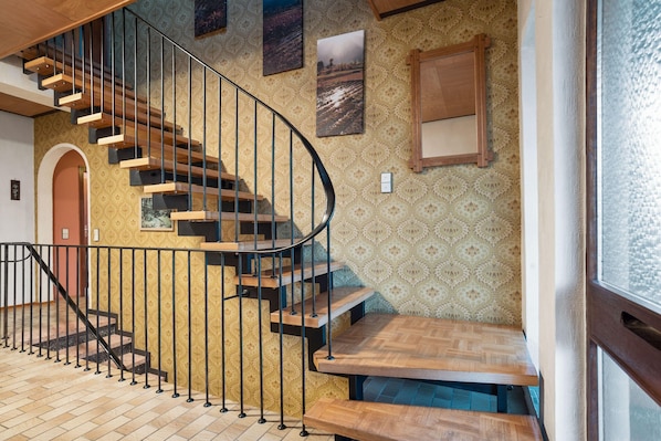 A spiral staircase with wooden steps and black railings, leading to a landing with a herringbone-patterned floor. - Holiday Home in Hesse with Infrared Sauna near Sauerland (Frankenau)