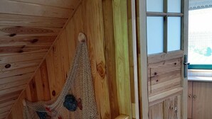 A wooden cabin interior with a sloped ceiling, a wooden staircase, and a window with a view of greenery.