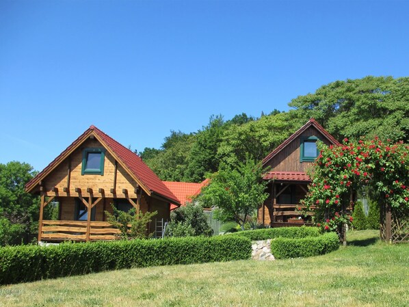 Two wooden cabins with red roofs, surrounded by well-maintained hedges and a stone wall.