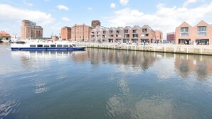 A waterfront area with a row of brick buildings, a blue boat docked at the pier, and a clear sky.