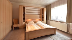 A bedroom with a bed, a chair, and built-in shelving.
