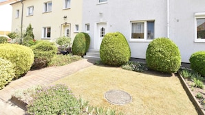 A two-story residential building with a well-maintained garden, including neatly trimmed hedges and a paved pathway.