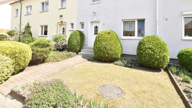 A two-story residential building with a well-maintained garden, including neatly trimmed hedges and a paved pathway.