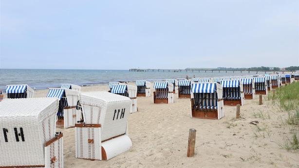 Beach huts with striped awnings, arranged in rows on a sandy beach, with the sea and a pier in the background. - Peaceful Apartment in Klütz Germany near Boltenhagener Beach (Klütz)
