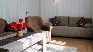 A living room with a brown armchair, a beige sofa with decorative pillows, and a white coffee table with a vase of red flowers.