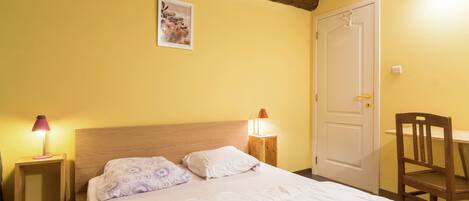 A bedroom with a wooden headboard, a bed with white bedding, two bedside lamps, a wooden chair, and a door.