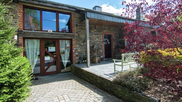 A stone building with a wooden deck, a bench, and a small garden area. - Quaint Apartment in Sensenruth With Terrace (Bouillon)