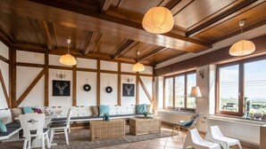 A spacious living area with a high ceiling, wooden beams, and large windows offering a view of the outdoors. - Gouvy Getaway Holiday Home (Gouvy)