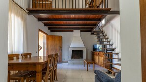 A spacious living area with a wooden dining table, chairs, a sofa, a fireplace, and a staircase. - Seaside Comfort in Giannella (Orbetello)