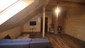 Un acogedor cuarto ático con techo inclinado, paredes de madera, chimenea, televisor y un sofá.