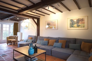 Un soggiorno con un divano grigio, travi in legno a soffitto e due quadri appesi al muro.