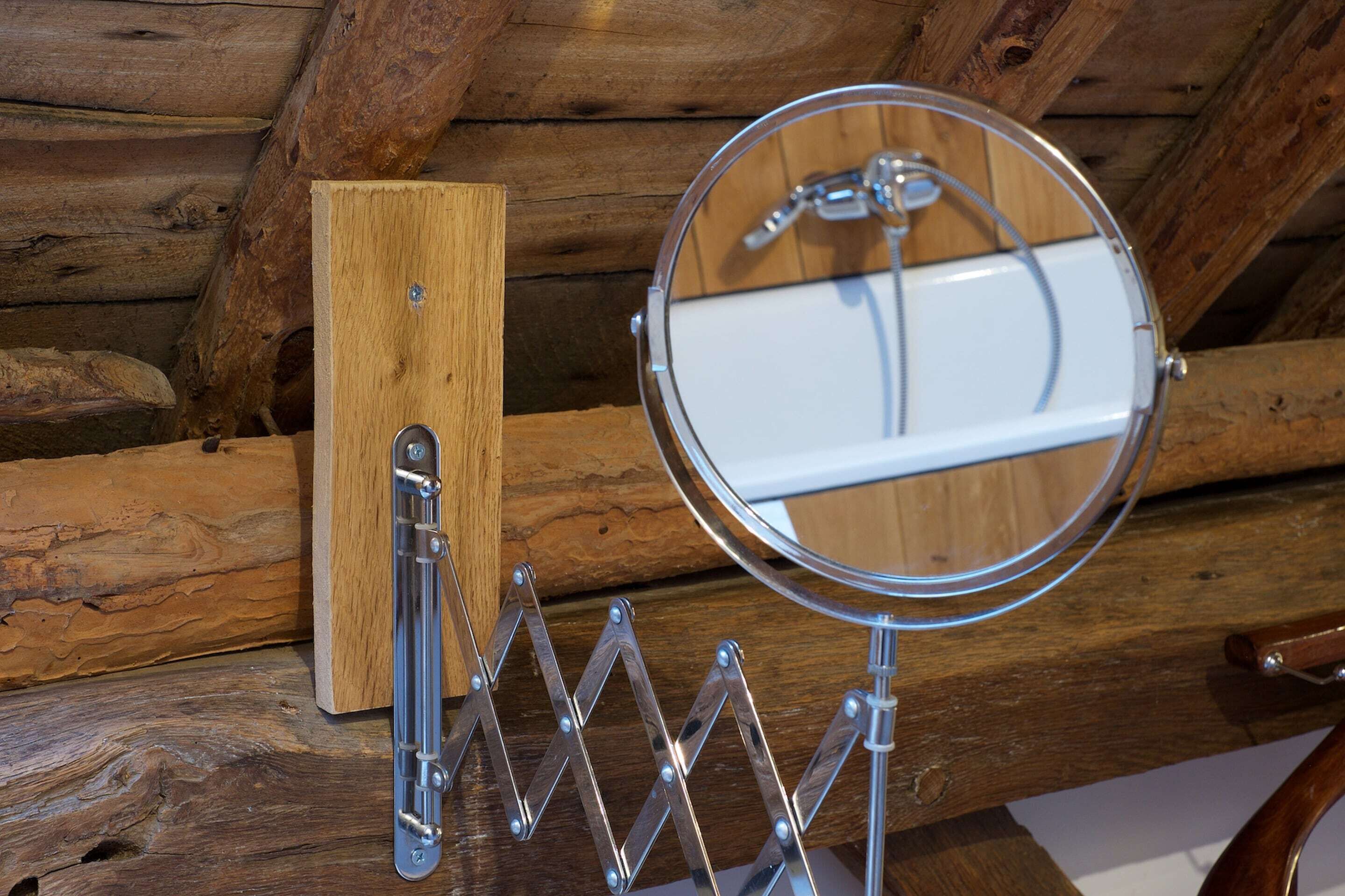A wooden log cabin interior with a metal-framed mirror and a wooden object on a shelf.