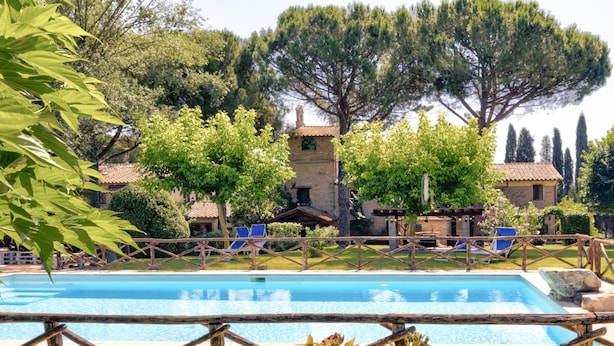 Piscina con sillas de descanso, rodeada de árboles y un edificio de piedra.