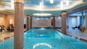 Una piscina interior lujosa con mosaicos, elegantes columnas y un techo decorativo.