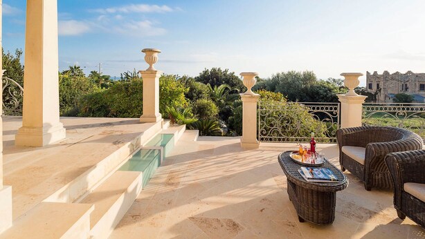 Una terraza con piscina, mobiliario exterior y vistas a vegetación y un edificio histórico.