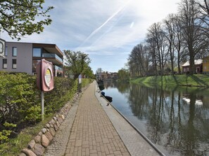 Une promenade au bord de la rivière, avec un chemin pavé, un canal et des bâtiments le long de la rive.