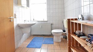 A small bathroom with a white sink, toilet, and a window. There is a wooden shelf with toiletries and a blue mat on the floor. - Lovely Apartment in Plau am See Germany near Plauer Lake (Plau am See)