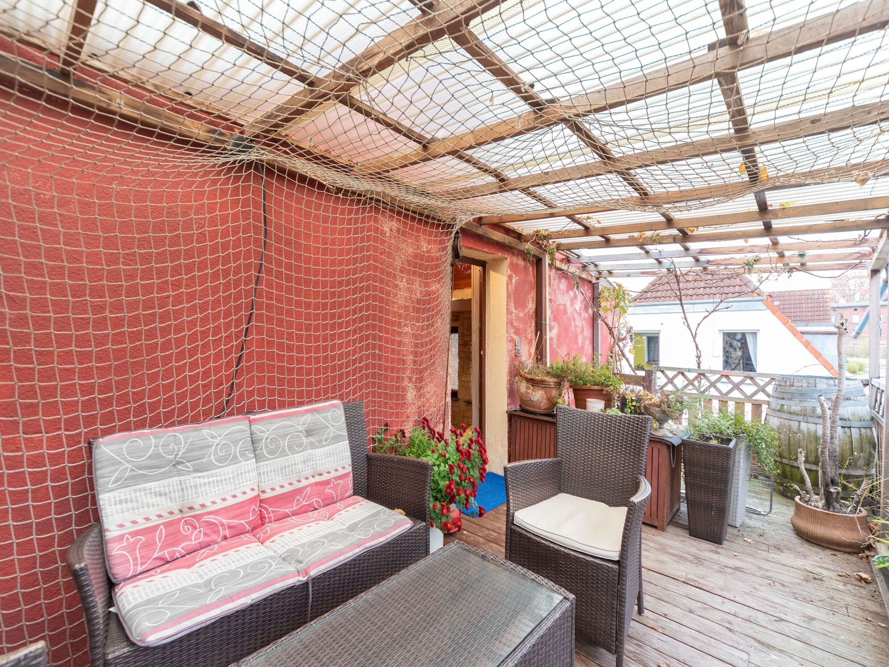 A covered patio area with wicker furniture, a red wall, and potted plants.