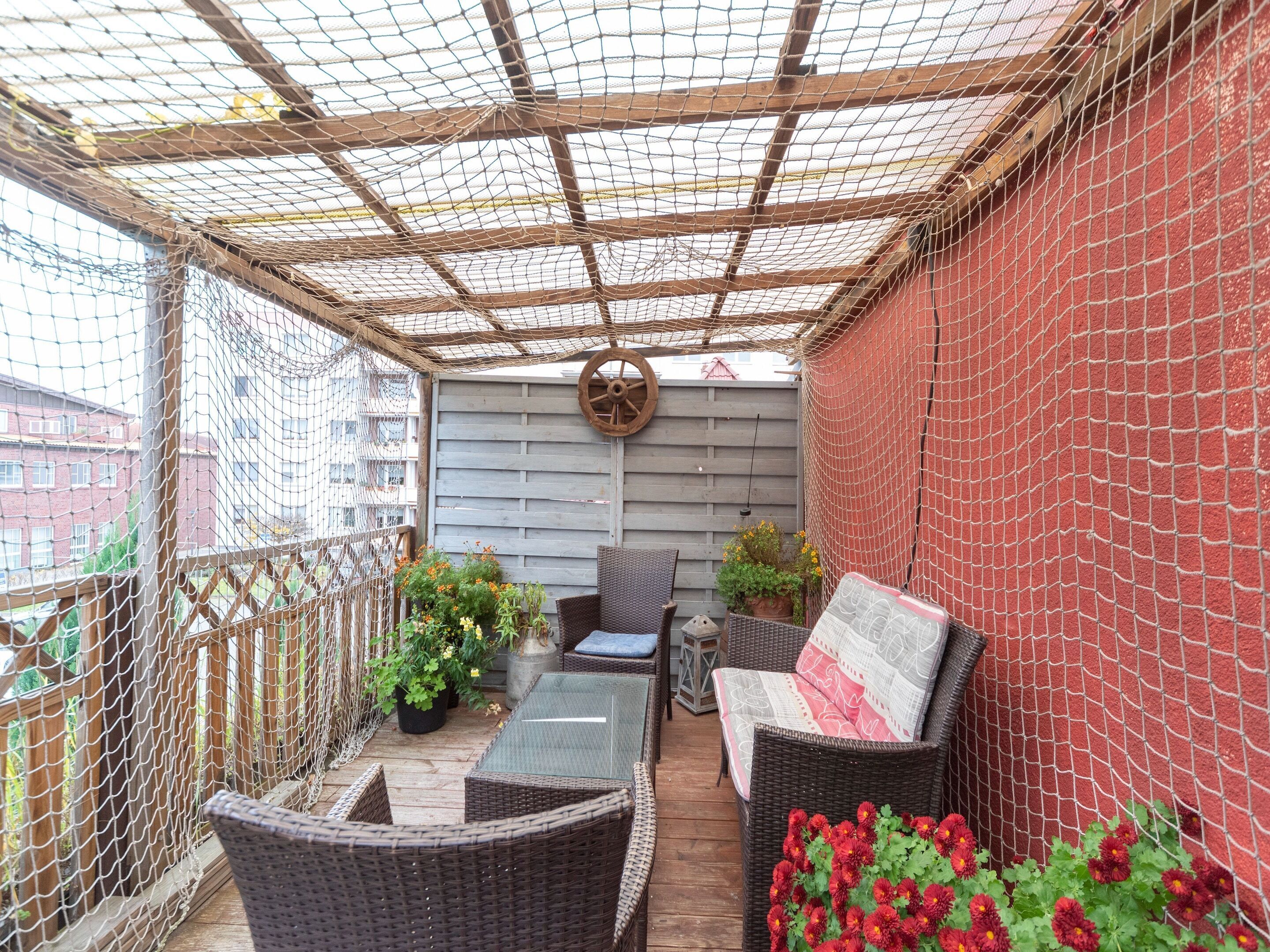 A covered outdoor seating area with wicker furniture, potted plants, and a wooden deck.