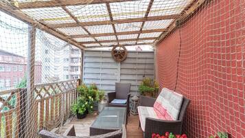 A covered outdoor seating area with wicker furniture, potted plants, and a wooden deck.