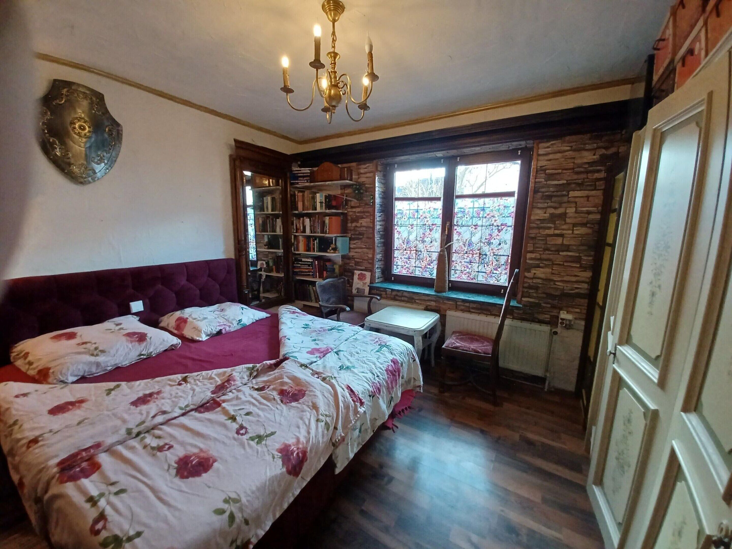 Ein Schlafzimmer mit einem großen Bett, einem kleinen Tisch, einem Stuhl, einem Bücherregal und einem Fenster mit Blick.