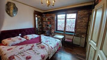 Ein Schlafzimmer mit einem großen Bett, einem kleinen Tisch, einem Stuhl, einem Bücherregal und einem Fenster mit Blick.