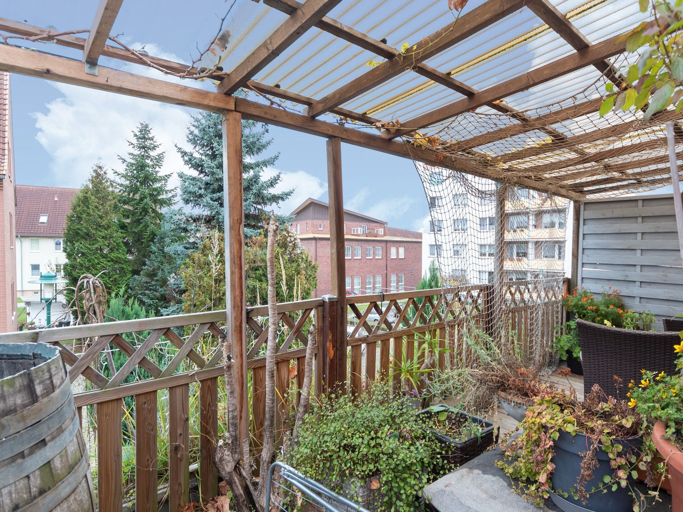A covered outdoor area with a wooden pergola, potted plants, and a view of residential buildings.