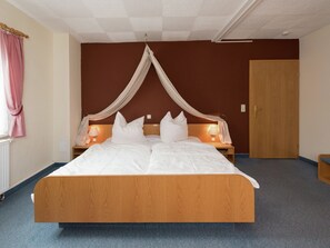 A bedroom with a four-poster bed, bedside lamps, a wooden door, and a radiator.