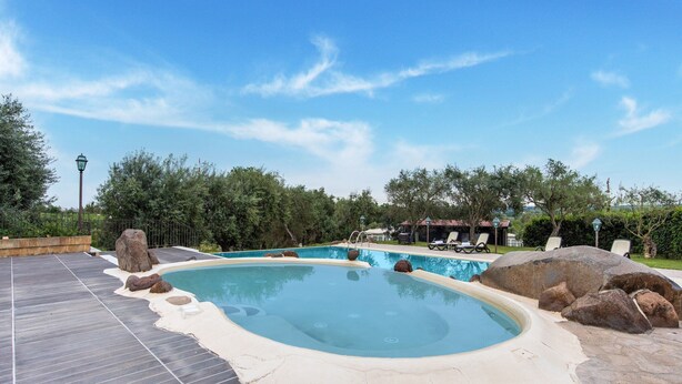 Een zwembad met een jacuzzi, omringd door rotsen en een terras met ligbedden.