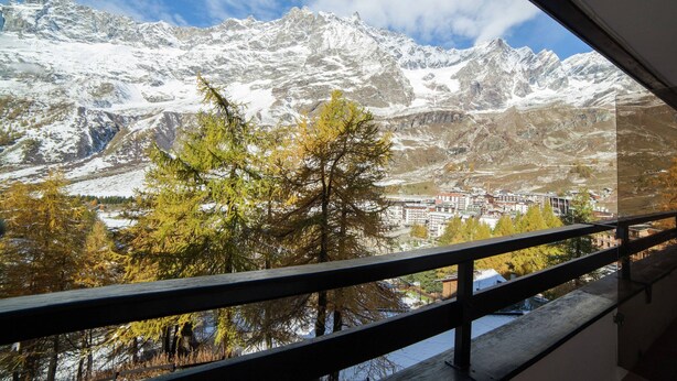 A mountain view from a balcony with a railing, snow-covered peaks, and a town below. - Near the Ski Lifts (Valtournenche)