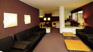 A hotel lobby with a brown patterned wall, a black sofa, a wooden coffee table, and a reception desk with a plant. - Near the Ski Lifts (Valtournenche)