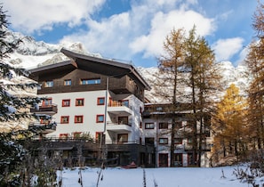 A multi-story hotel with balconies, a ski lift, and snow-covered mountains in the background.