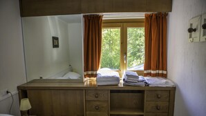 A wooden dresser with a mirror, a bed with white bedding, and a window with curtains. - Near the Ski Lifts (Valtournenche)