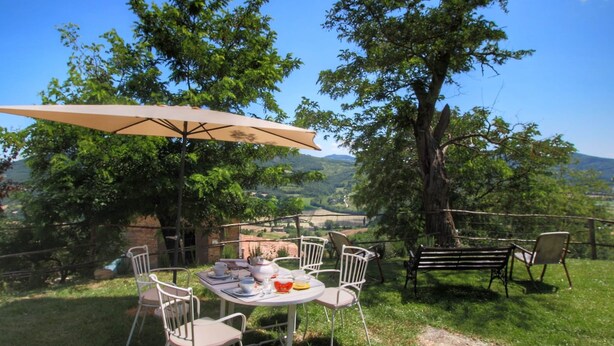An outdoor dining area with a table and chairs, surrounded by trees and a scenic view of hills. - Farmhouse in Umbertide Near Lake Trasimeno (Umbertide)