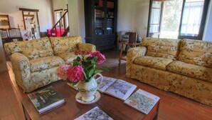 A living room with two floral sofas, a coffee table with books and a vase of flowers, and a dark wooden bookshelf. - Farmhouse in Umbertide Near Lake Trasimeno (Umbertide)