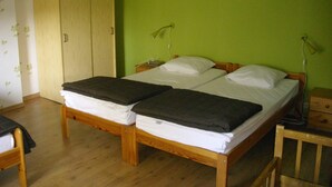 Quarto com duas camas de madeira, um guarda-roupa e uma escrivaninha com abajur.