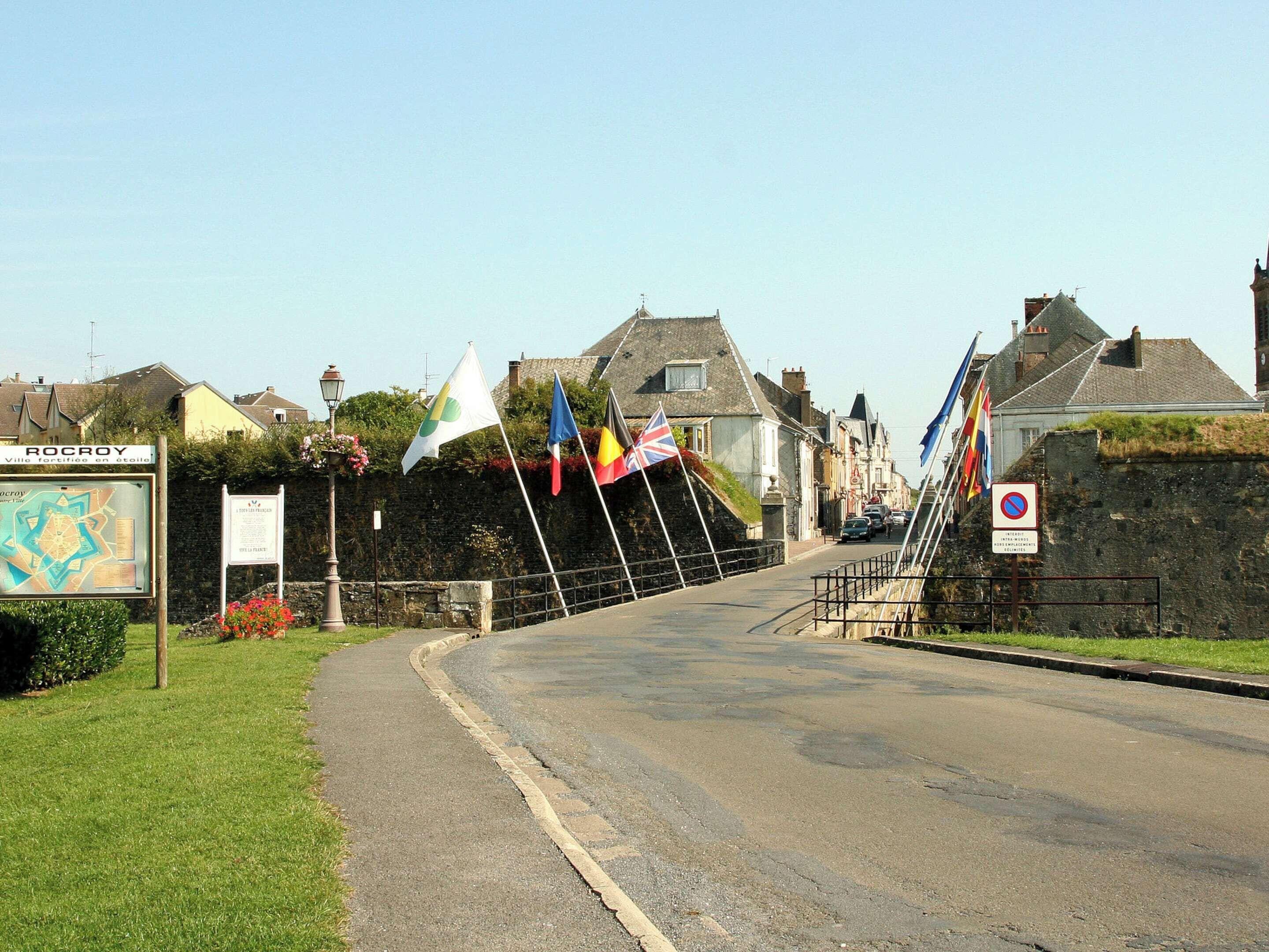 A street with flags, a signboard, and a stone wall.