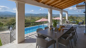 Un espacio de comedor al aire libre techado con vista a la piscina, techo de madera y mobiliario exterior.