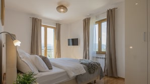 Un dormitorio con cama, lámpara de noche, televisor y una planta en maceta.
