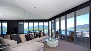 Een moderne woonkamer met een grote bank, een glazen salontafel en uitzicht op water en bergen.