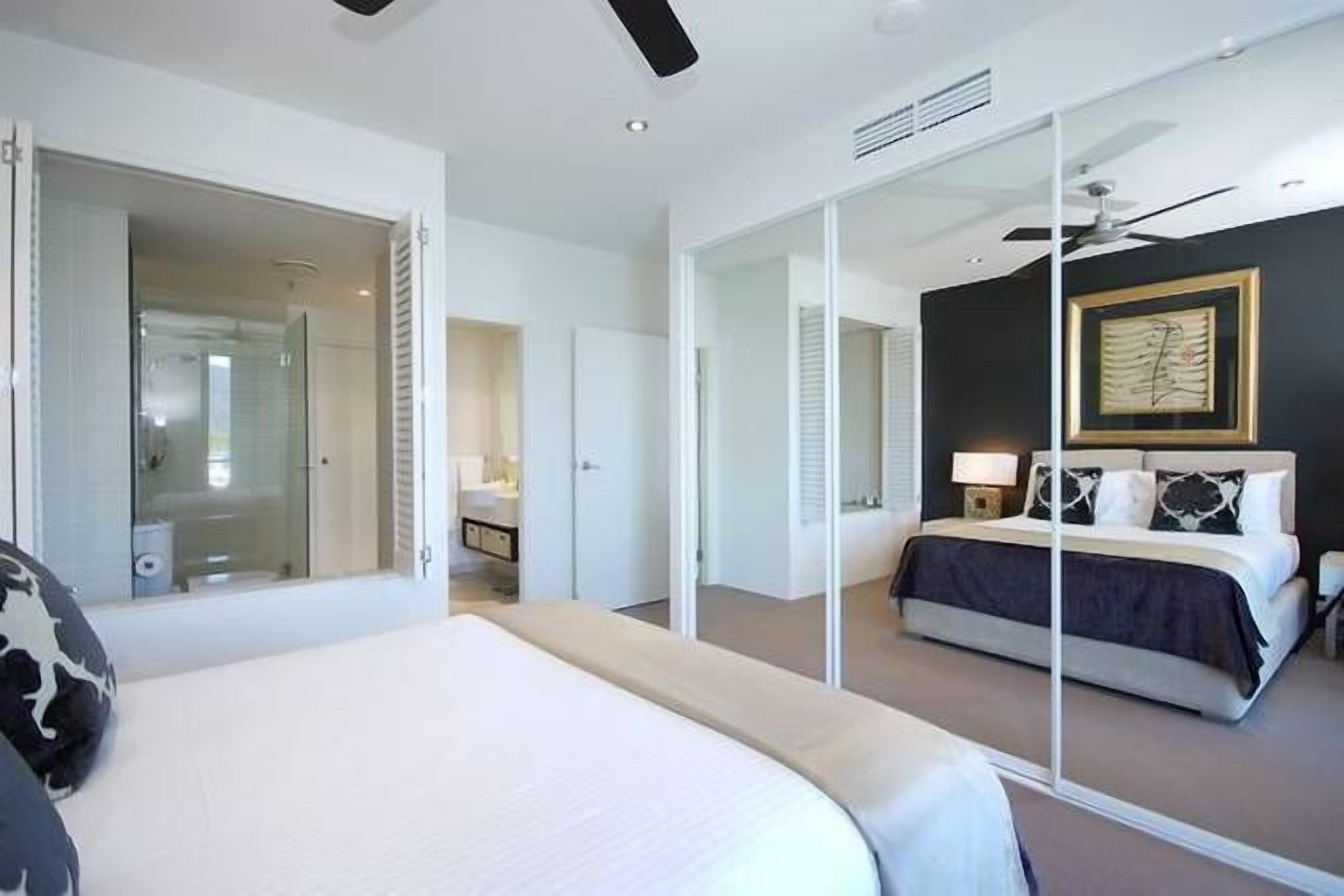 A modern hotel room with a large bed, a separate sitting area, a glass partition, and a ceiling fan.