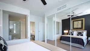 Een moderne hotelkamer met een groot bed, een afzonderlijke zithoek, een glazen scheidingswand en een plafondventilator.