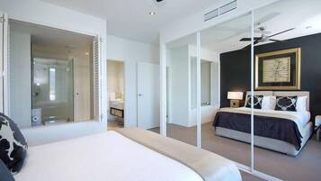 A modern hotel room with a large bed, a separate sitting area, a glass partition, and a ceiling fan.