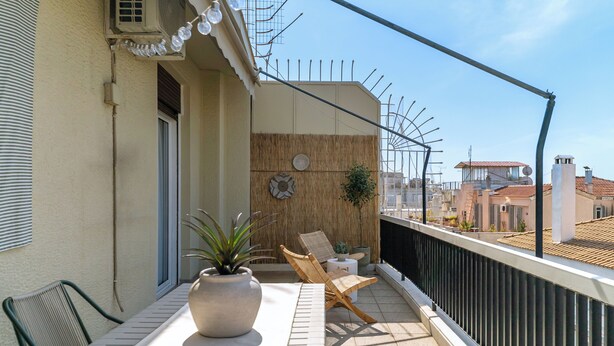 Un balcón con mesa, sillas, plantas en macetas y vistas a edificios.