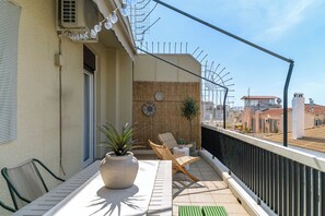 Un balcón con mesa, sillas, plantas en macetas y vistas a edificios.
