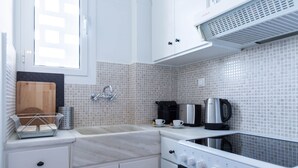 Una cocina compacta con armarios blancos, un lavamanos, una cafetera y un hervidor.