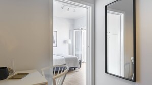 Una habitación de hotel moderna con un espejo grande, una cama, un escritorio con silla y vistas a la habitación contigua.