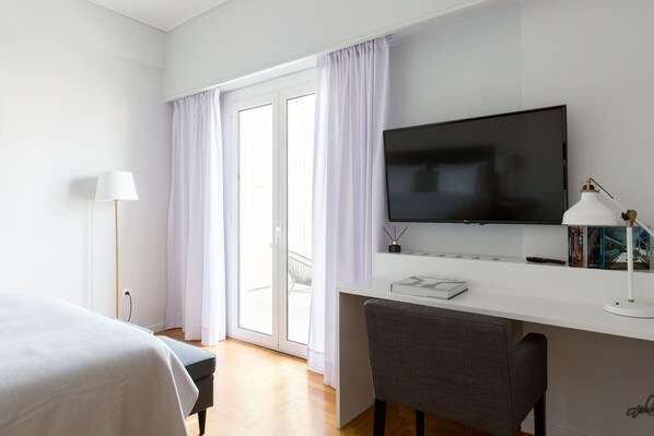 Habitación de hotel con cama, escritorio con silla, televisor, lámpara y ventana con cortinas.